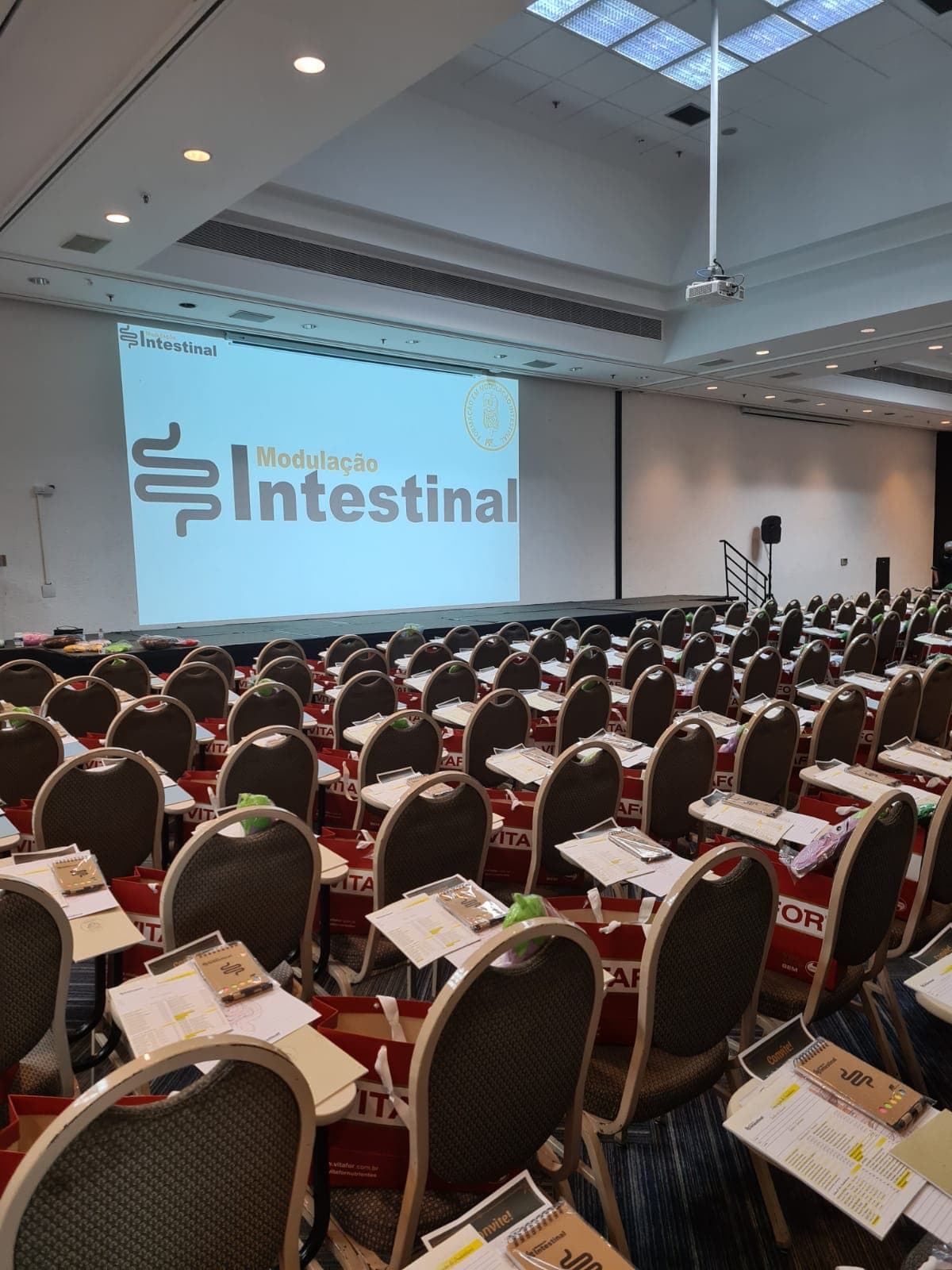 Auditório preparado para o curso, com kits de material sobre as cadeiras